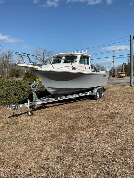 Slide: The Image of 2025 Parker 2120 Sport Cabin boat on trailer, parked on grass under clear blue sky. - 1