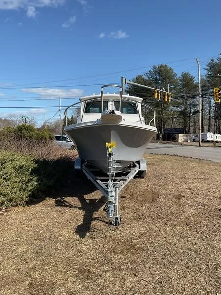 Slide: The Image of 2025 Parker 2120 Sport Cabin boat on trailer, parked on grass near road. - 2