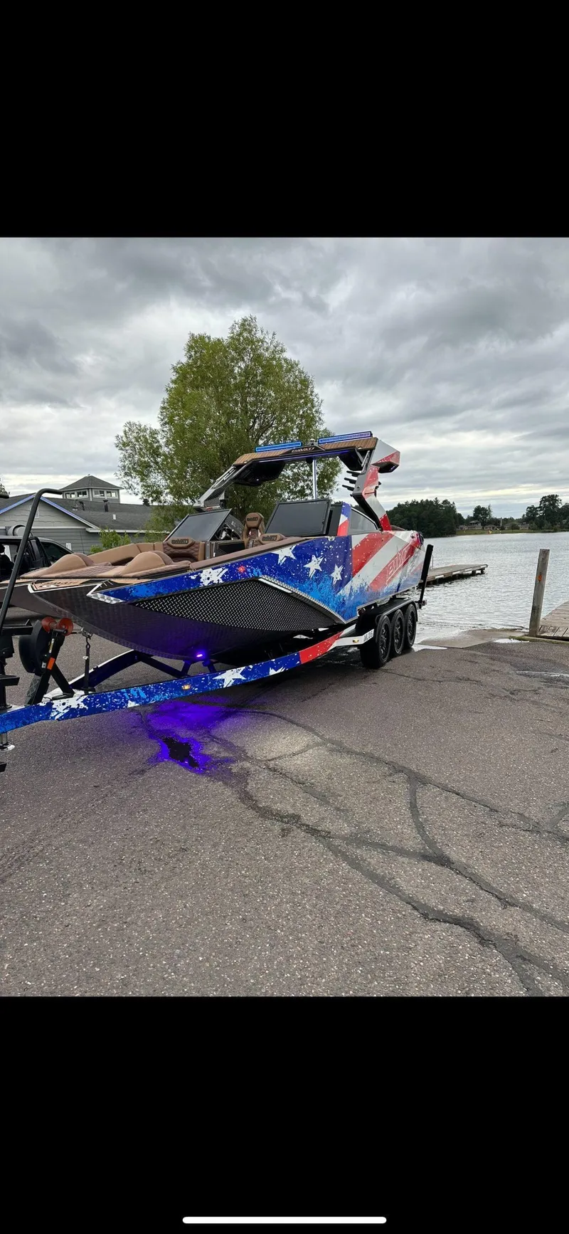 Slide: The Image of 2022 Pavati AL26 boat with American flag design on a trailer by a lake. - 2