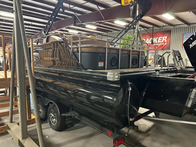 Slide: The Image of 2025 Regency 250 LE3 Sport pontoon boat in showroom, black exterior, on trailer. - 2