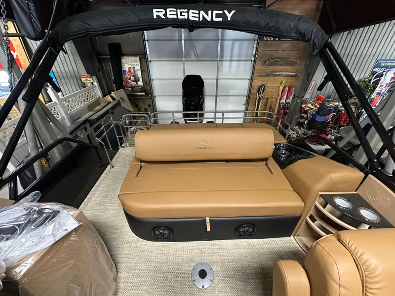 Slide: The Image of 2025 Regency 250 LE3 Sport boat interior with tan seating and cup holders in a showroom. - 7