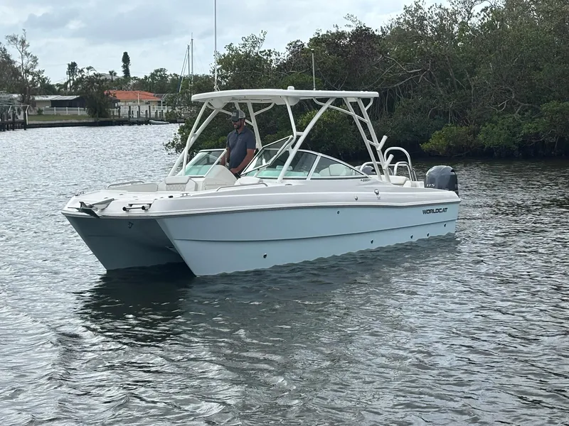 Slide: The Image of 2025 World Cat 230 SD boat on calm water near lush greenery. - 2