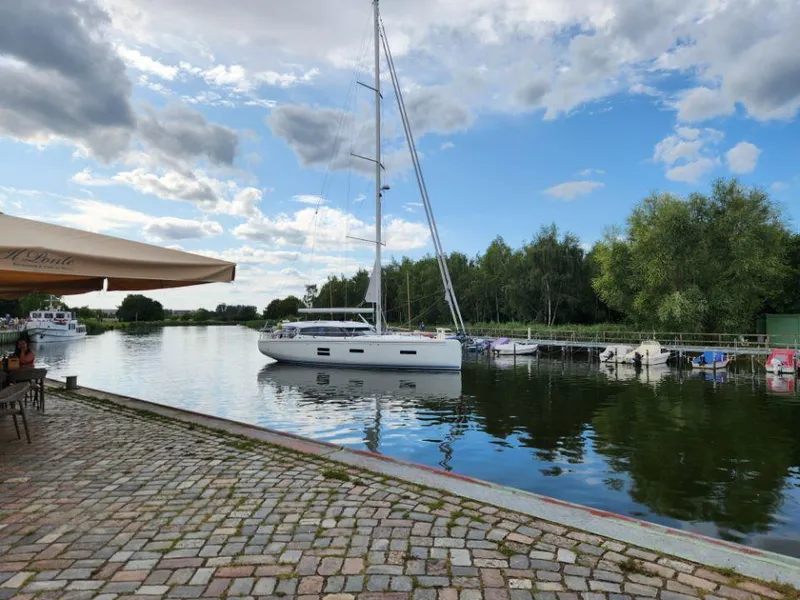 Slide: The Image of Sailboat Moody 48 DS 2025 docked by a scenic riverside under a partly cloudy sky. - 6