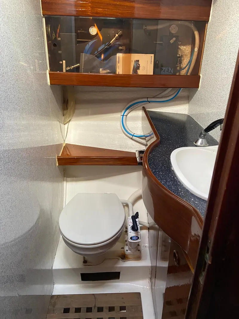 Slide: The Image of 1984 Beneteau First 42 yacht bathroom with toilet, sink, and wooden shelves. - 48