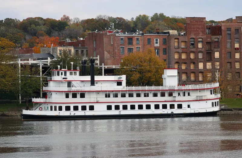 The Image of Vintage 1985 custom passenger boat docked by historic brick buildings in autumn. - 0