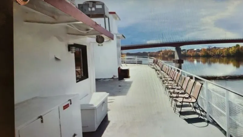 Slide: The Image of 1985 custom passenger boat deck with chairs, river view, and bridge in the background. - 3