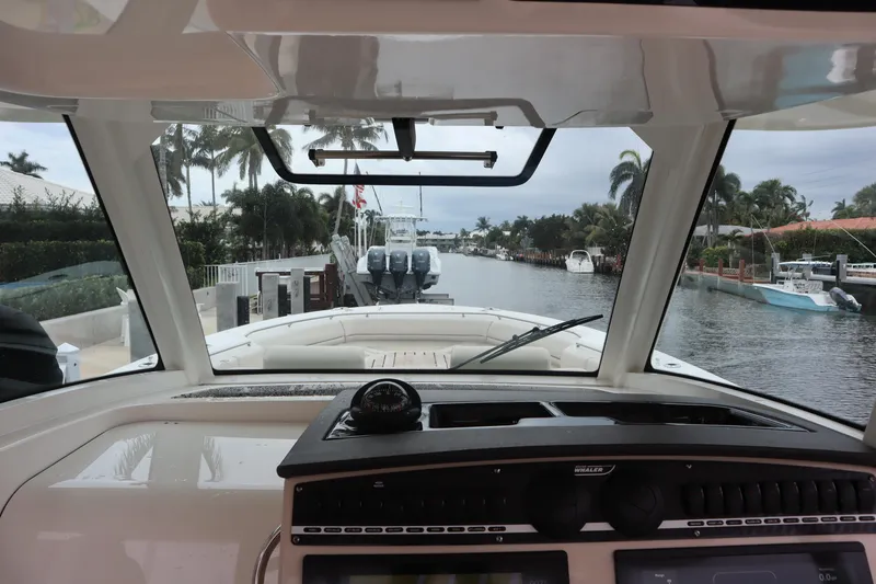 Slide: The Image of 2022 Boston Whaler 380 Outrage cockpit view, navigating a scenic canal with palm trees. - 22