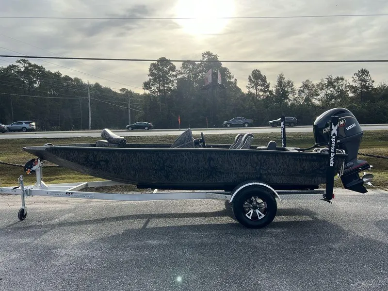 The Image of 2025 Xpress H18 Bass boat on trailer, parked outdoors under cloudy sky. - 1