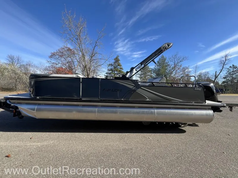 Slide: The Image of 2024 Avalon LSZ Versatile Rear Bench pontoon boat on pavement, clear sky background. - 5