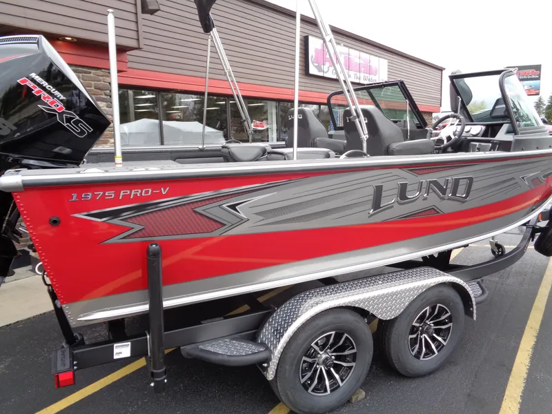 Slide: The Image of 2025 Lund 1975 Pro-V boat, red and gray, on a trailer outside a building. - 6