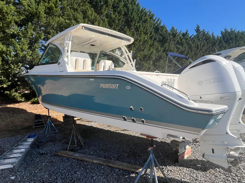 Slide: The Image of 2017 Pursuit 325 DC Dual Console boat on stands, blue hull, outdoor setting. - 10