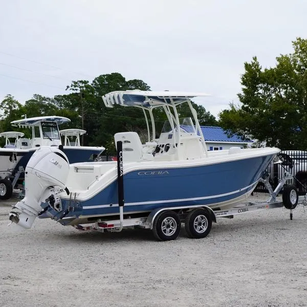 Slide: The Image of 2025 Cobia 220 Center Console boat on trailer, blue and white design. - 2