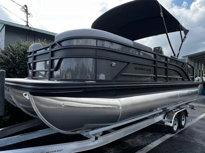 Slide: The Image of 2025 Bennington S 22 pontoon boat on trailer with canopy, parked outdoors. - 2