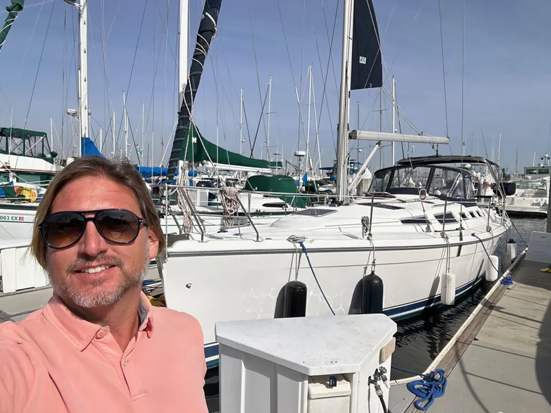 Slide: The Image of Man smiling in front of a 2008 Hunter 38 sailboat docked at a marina. - 1