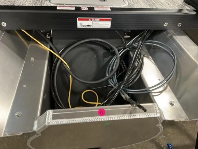 Slide: The Image of Bennington 23 SL 2025 boat compartment with cables and warning label. - 15