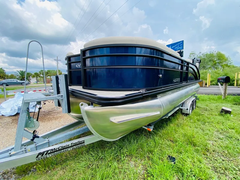 Slide: The Image of 2023 Harris Cruiser 230 pontoon boat on trailer, parked on grass under cloudy sky. - 3