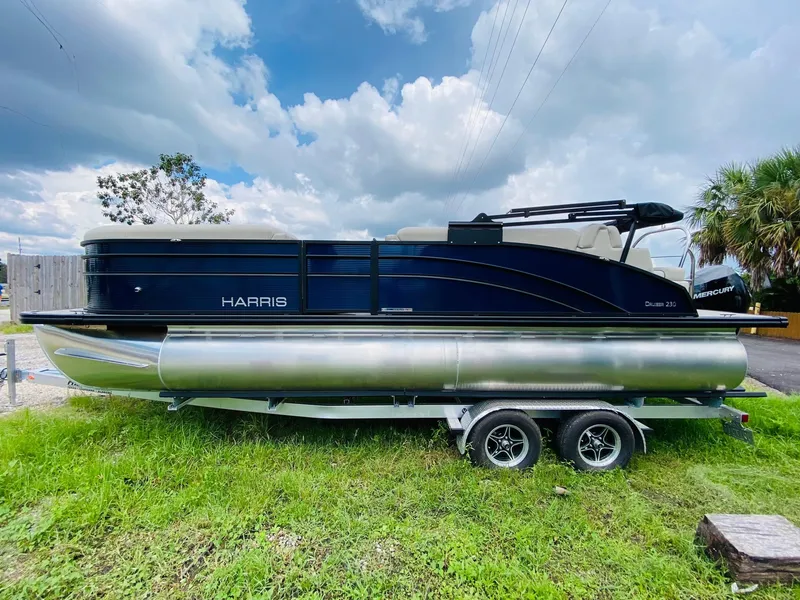 Slide: The Image of 2023 Harris Cruiser 230 pontoon boat on trailer, parked on grass under cloudy sky. - 4