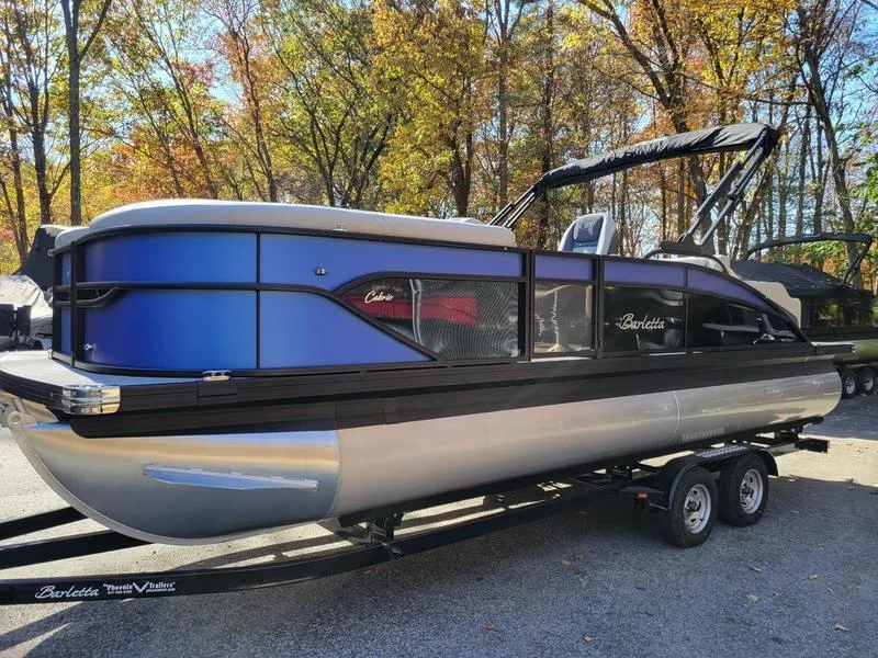 Slide: The Image of 2025 Barletta C22UC pontoon boat on trailer, surrounded by autumn trees. - 1
