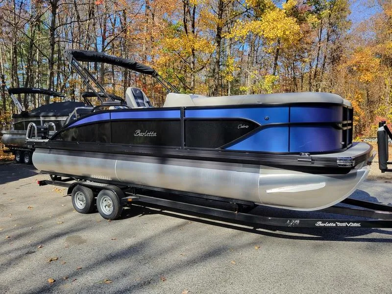 Slide: The Image of 2025 Barletta C22UC pontoon boat on trailer, parked in wooded area. - 4