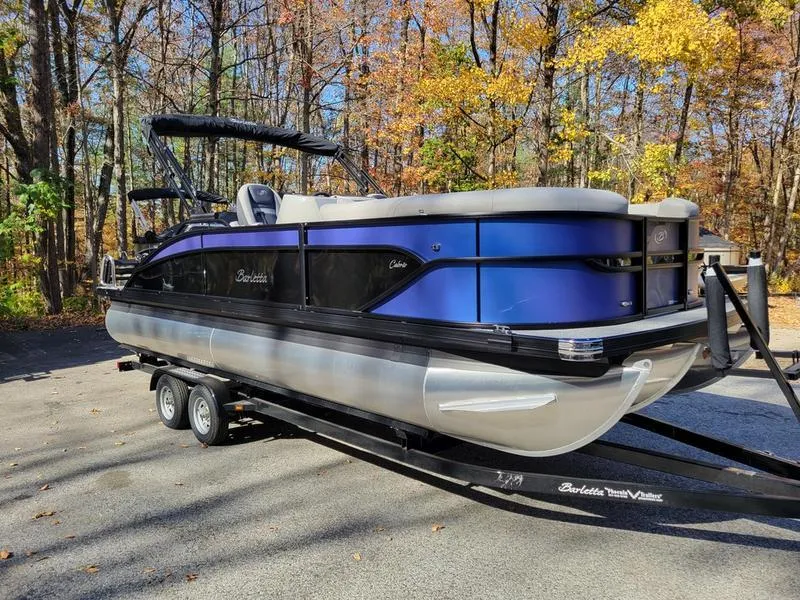 Slide: The Image of 2025 Barletta C22UC pontoon boat on trailer, parked in wooded area. - 5