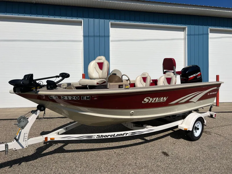 Slide: The Image of 1997 Sylvan 1600 Pro Select fishing boat on ShoreLand'r trailer, parked outside blue building. - 15