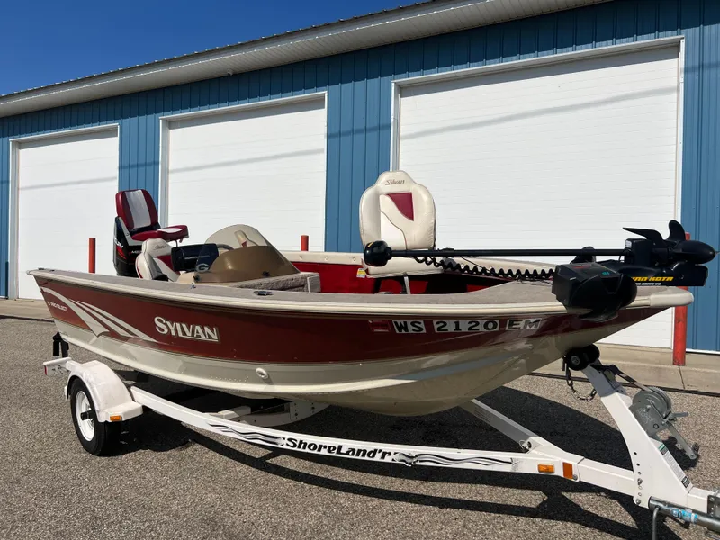 Slide: The Image of 1997 Sylvan 1600 Pro Select fishing boat on trailer, parked near blue storage units. - 3