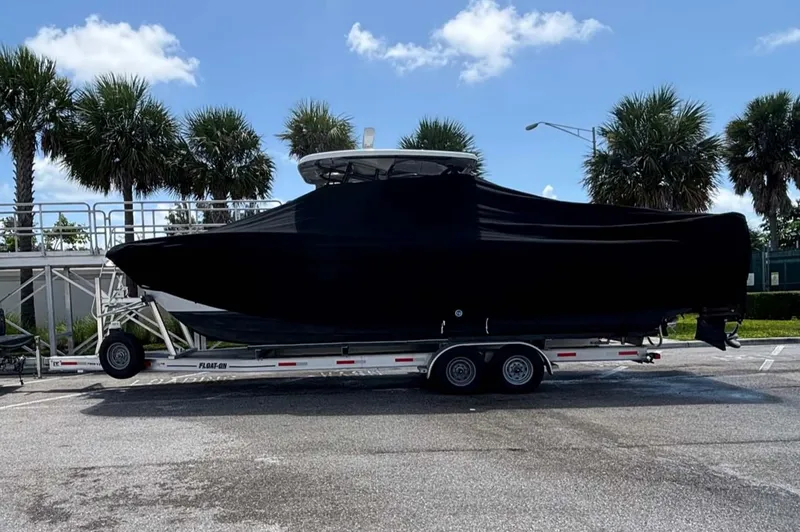 Slide: The Image of 2023 Twin Vee 280 GFX CC boat covered on a trailer, parked near palm trees. - 32