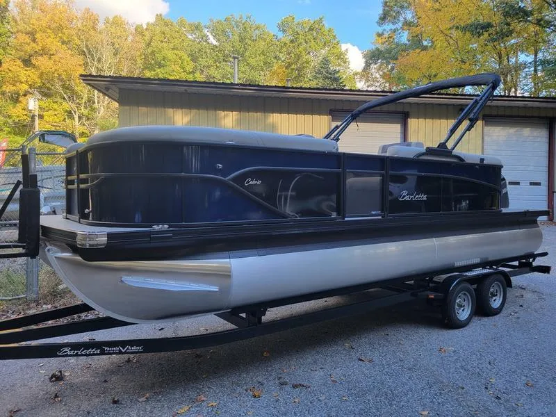 Slide: The Image of 2025 Barletta C22Q pontoon boat on trailer, parked outdoors. - 1