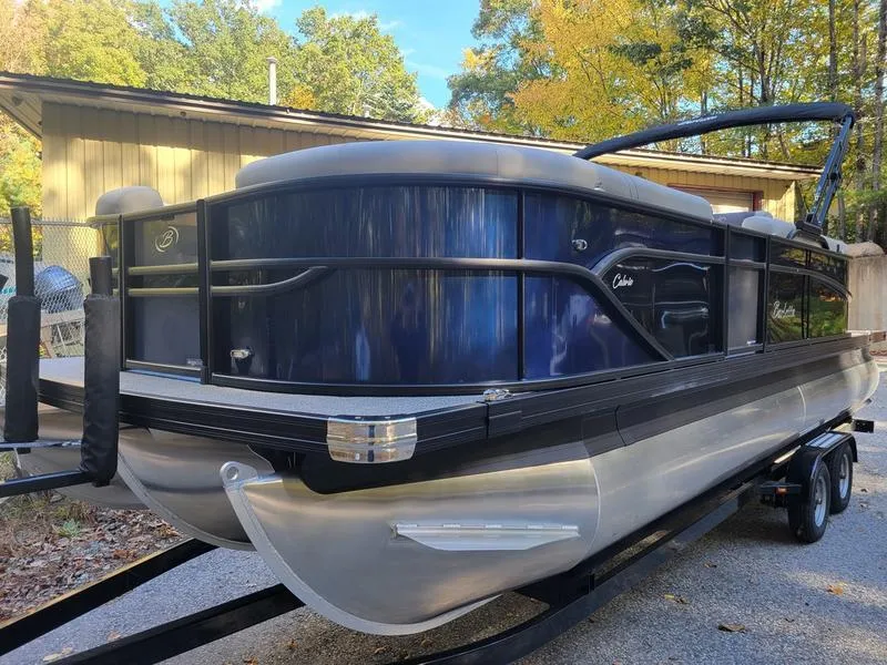 Slide: The Image of 2025 Barletta C22Q pontoon boat on trailer, parked outdoors with trees in background. - 2