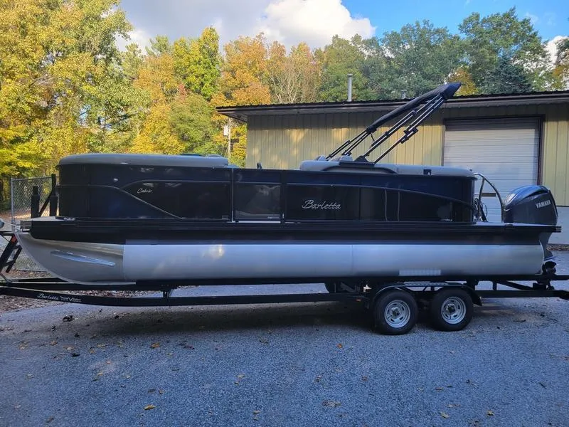 Slide: The Image of 2025 Barletta C22Q pontoon boat on trailer, parked outdoors near trees and building. - 3