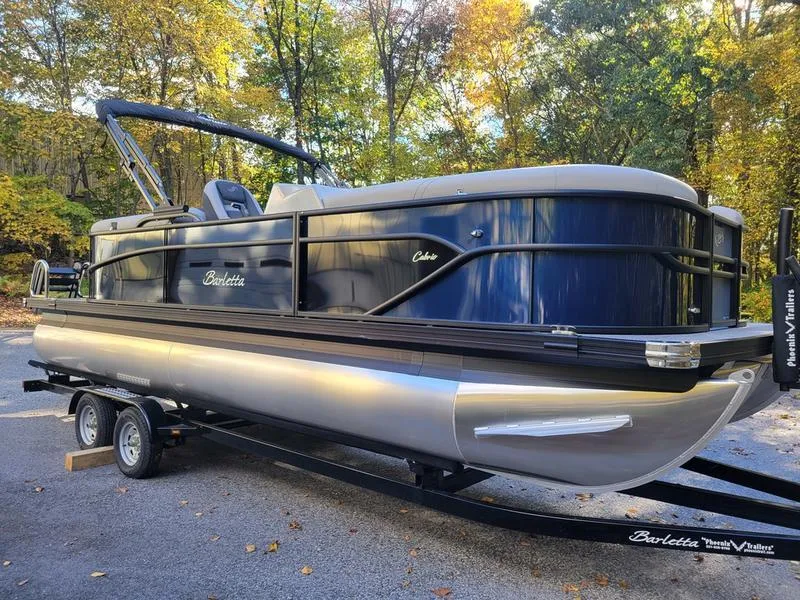 Slide: The Image of 2025 Barletta C22Q pontoon boat on trailer, parked outdoors with autumn trees. - 4