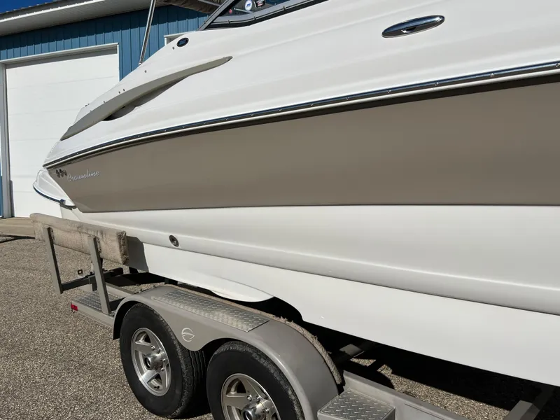 Slide: The Image of 2006 Crownline 260 LS boat on trailer, side view, parked near a blue building. - 27