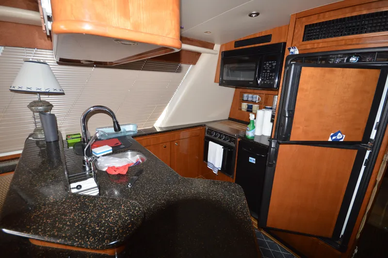 Slide: The Image of 2007 Meridian 490 Pilothouse kitchen with wood cabinetry, black countertops, and modern appliances. - 19