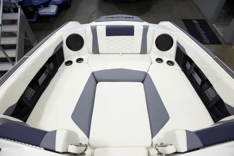 Slide: The Image of 2025 Malibu 24 MXZ boat interior with white and gray seating and built-in speakers. - 18