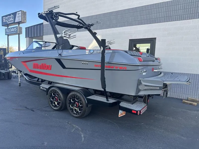 Slide: The Image of 2024 Malibu 23 MXZ boat on trailer, gray with red accents, parked outside dealership. - 4