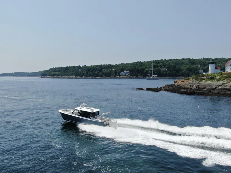 Slide: The Image of 2023 MJM 4 boat cruising near a rocky coastline with a lighthouse. - 2