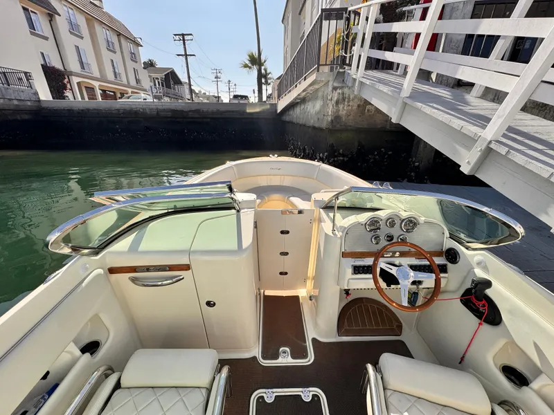 Slide: The Image of 2014 Chris-Craft Launch 25 boat interior with steering wheel and seating, docked near waterfront homes. - 5