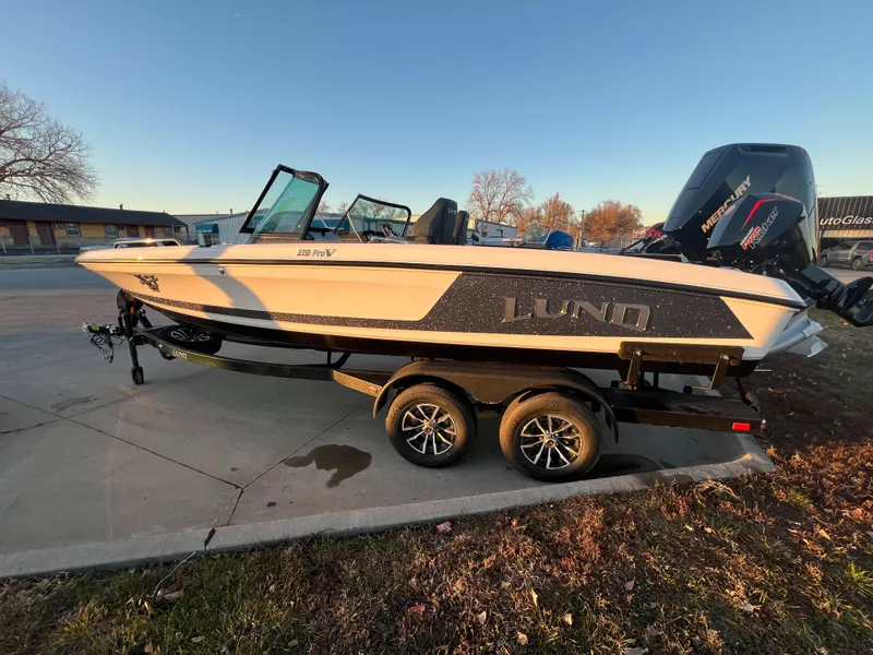 Slide: The Image of 2025 Lund 219 Pro-V GL boat on trailer, parked outdoors. - 2