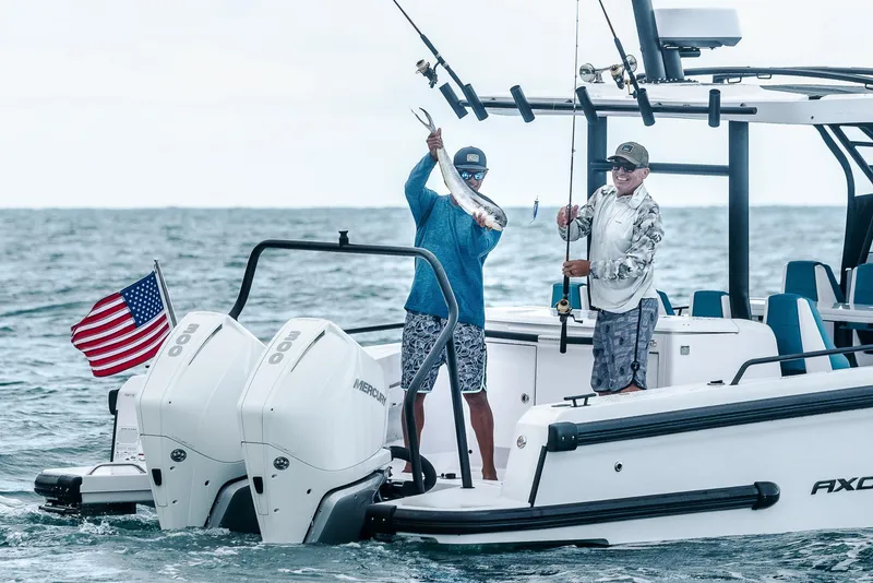 Slide: The Image of 2023 Axopar 28 T-Top boat with two people fishing, American flag, and twin engines. - 4