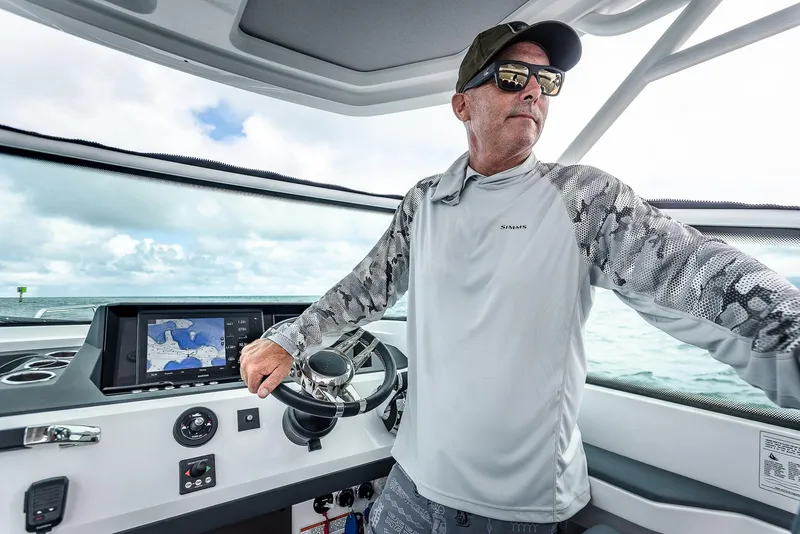 Slide: The Image of Man steering 2023 Axopar 28 T-Top boat, wearing sunglasses and cap, with navigation screen visible. - 6
