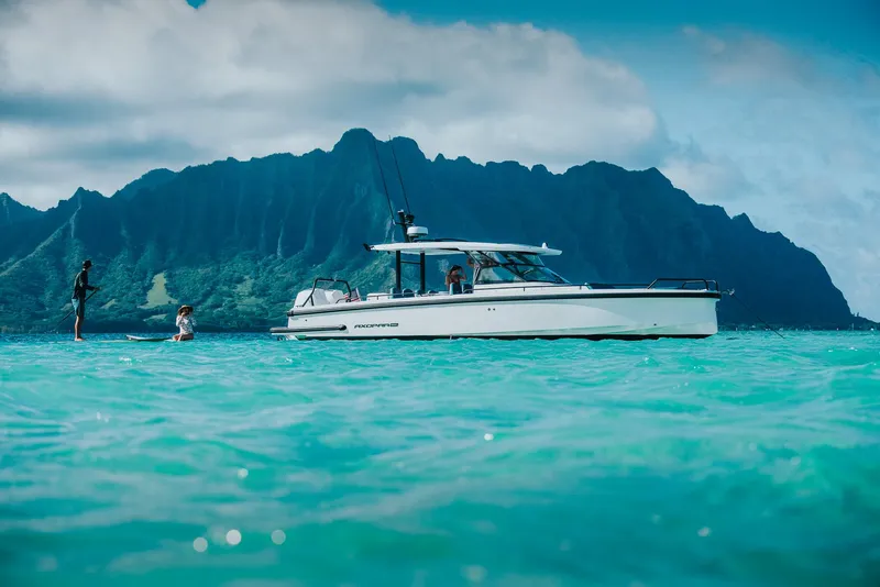 Slide: The Image of 2023 Axopar 37 Sun-Top Wet Bar on turquoise water with scenic mountain backdrop. - 13