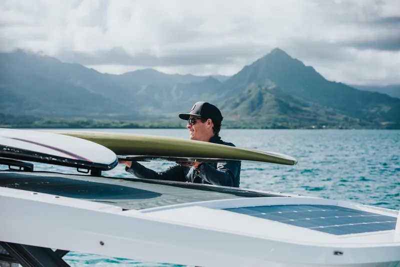 Slide: The Image of Man securing surfboard on 2023 Axopar 37 Sun-Top Wet Bar boat, scenic mountain backdrop. - 3