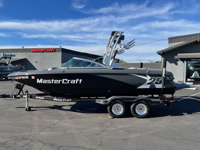 Slide: The Image of 2012 MasterCraft X25 boat on trailer, parked outdoors under blue sky. - 1
