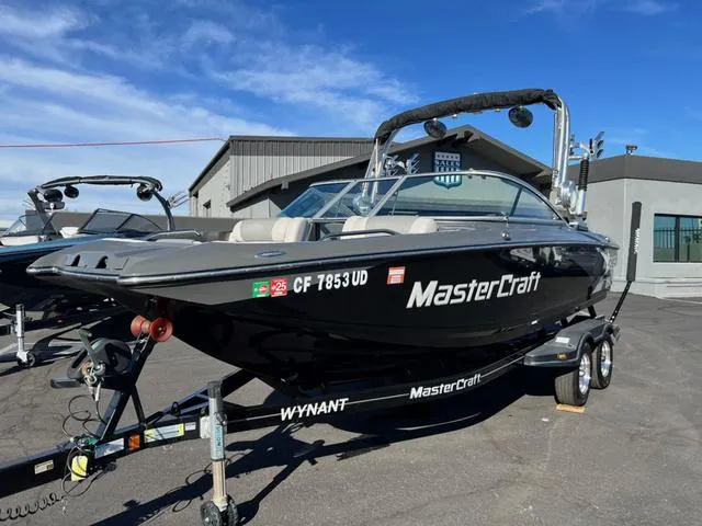 Slide: The Image of 2012 MasterCraft X25 boat on trailer, parked outdoors under clear sky. - 2