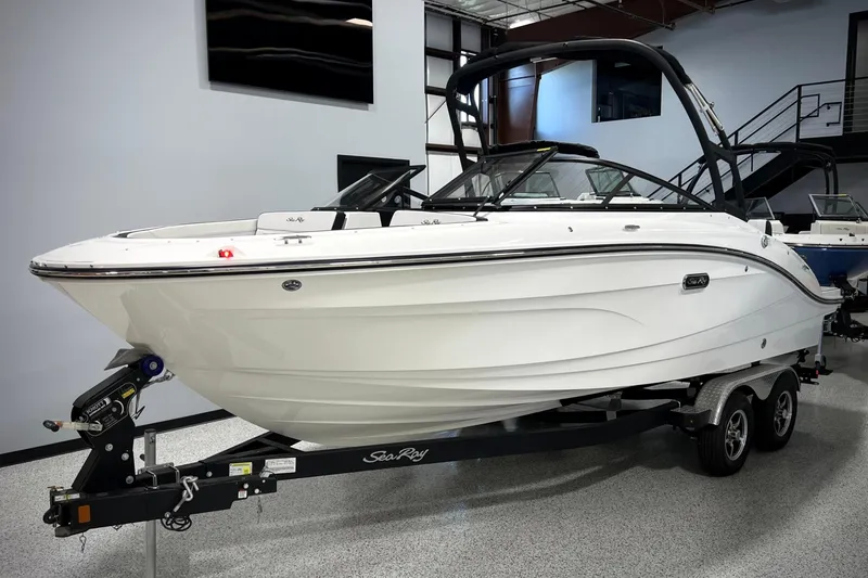 The Image of 2025 Sea Ray SPX 210 boat on trailer in showroom, sleek white design. - 0