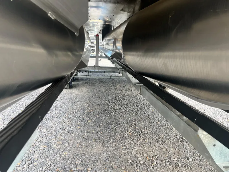 Slide: The Image of Underneath view of 2025 Sylvan L3 DLZ Tritoon, showcasing pontoons and trailer on gravel. - 7