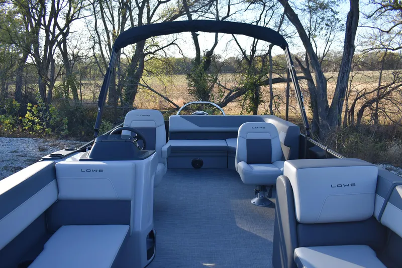 Slide: The Image of 2025 Lowe LS 190 pontoon boat interior with seating, set against a wooded backdrop. - 2