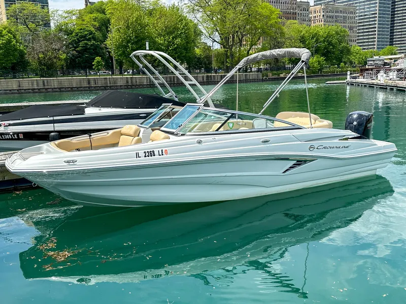 Slide: The Image of 2023 Crownline 215 XS boat docked on a serene lake with lush greenery. - 17