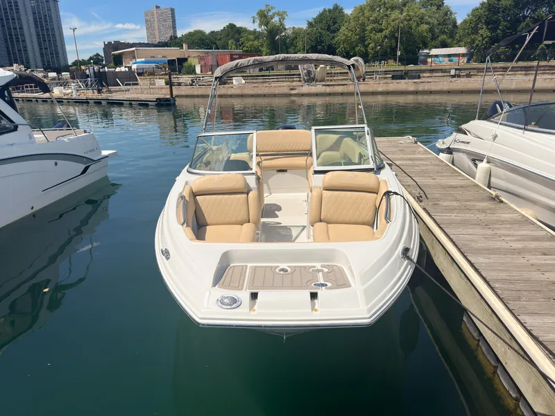 Slide: The Image of 2023 Crownline 215 XS boat docked in a marina, featuring beige seating and sleek design. - 5