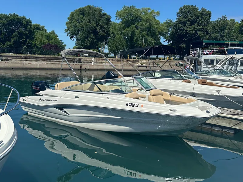 Slide: The Image of 2023 Crownline 215 XS boat docked in a marina, surrounded by trees and other boats. - 7